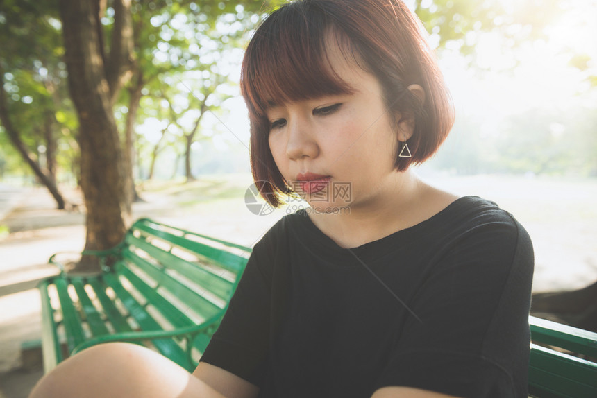 独自坐在公园席上的年轻女独自坐在公园席上周围充满自然和温暖的阳光图片