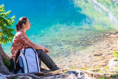 旅游业崇拜者背着包的旅行者坐在湖边塔特拉山上的摩尔斯基奥科湖边背着包的旅行者坐在湖边摩尔斯基奥科湖边背景