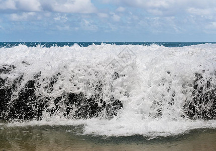 强烈的冲浪和波过卢马海滩的岩石冰冻得看起来像牛奶背景图片