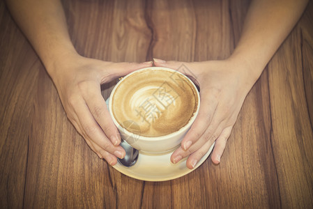 手握着咖啡杯在木制桌上图片