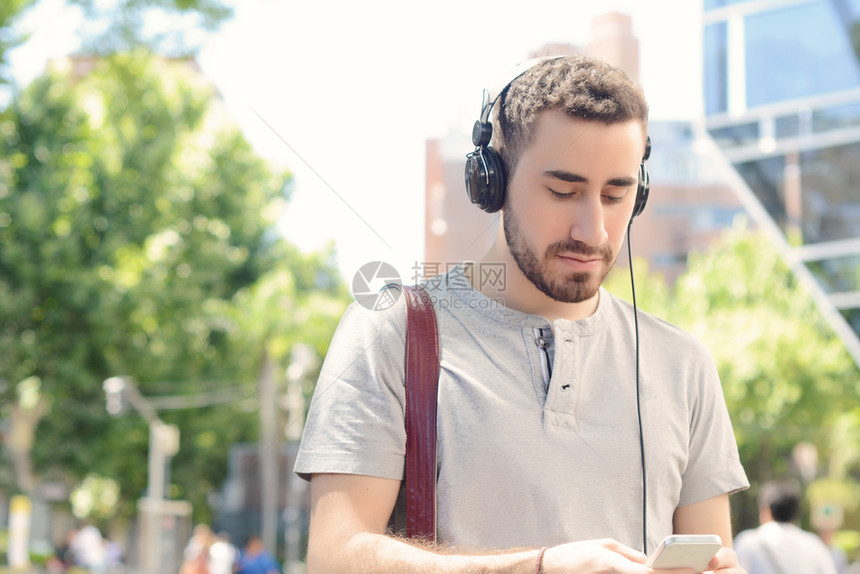 年轻拉丁男子用黑耳机在手上打字的肖像户外图片