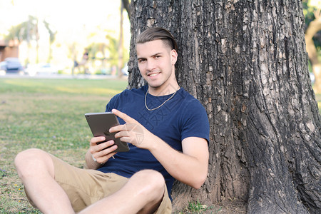 有吸引力的年轻人在公园户外使用带耳机的平板电脑图片