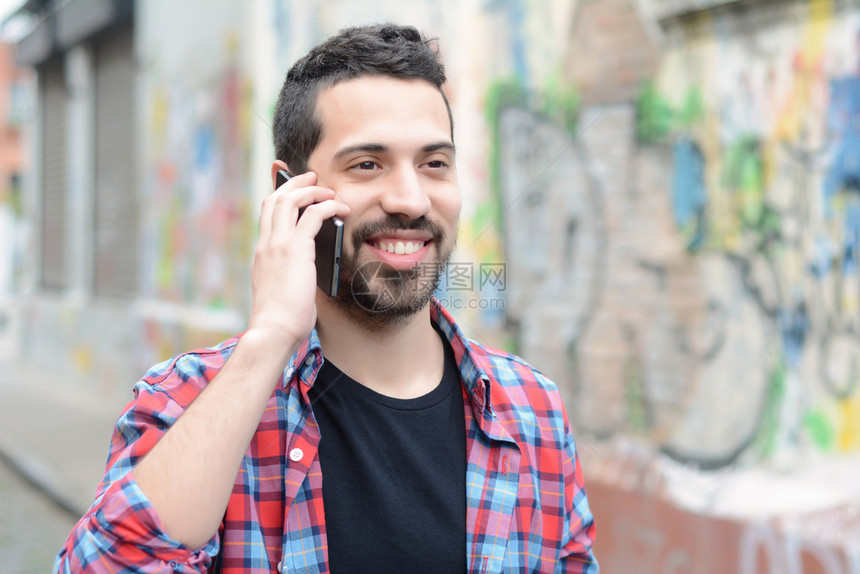 英俊的拉丁年轻人在电话里聊天潮流和城市风景图片