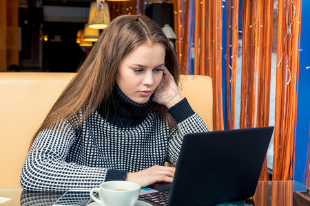 在咖啡馆工作手持笔记本电脑喝咖啡的年轻美女图片