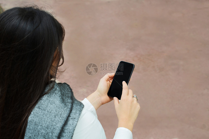 年轻女子拿着智能手机用手指着镜头在户外图片