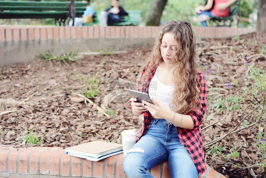 秋天在公园里坐着一块平板和个可支配咖啡杯的女学生图片