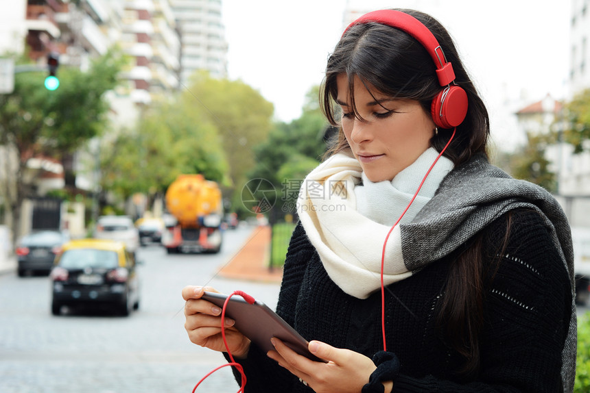 一位年轻美女用红耳机使平板户外城市风景的肖像图片