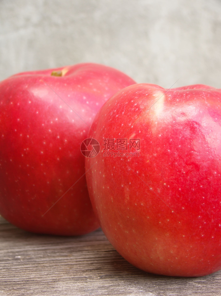 两个成熟的红苹果放在木制桌边的水泥墙上图片
