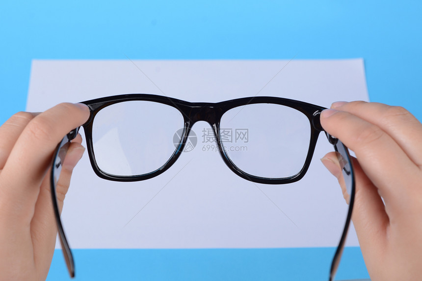 女手中的眼镜放在空白纸上聚焦于眼镜浅蓝色背景图片