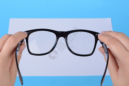女手中的眼镜放在空白纸上聚焦于眼镜浅蓝色背景图片