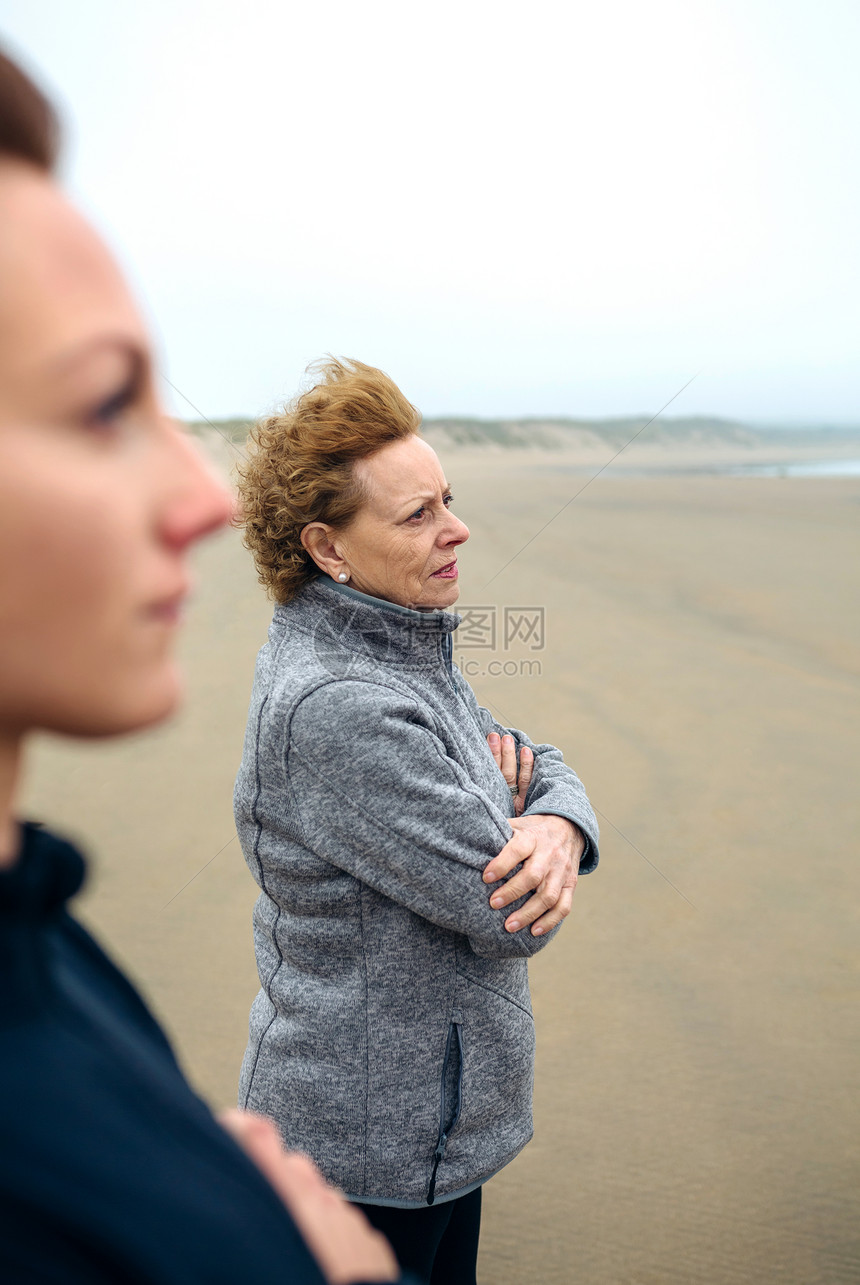 秋天在海滩上看的两名妇女有选择地关注背景中的妇女图片