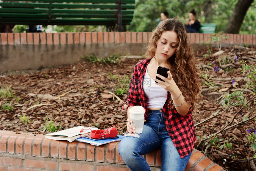 秋天在公园里坐着一块平板和个可支配咖啡杯的女学生图片