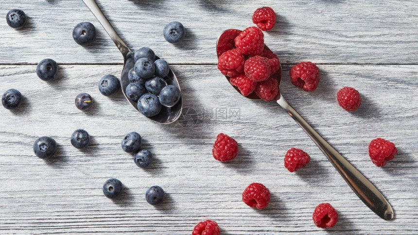 灰色背景的有机成熟新鲜莓和草健康干净的饮食平铺两勺子红色多汁的成熟浆果草莓和蓝周围是灰色木质背景的图片