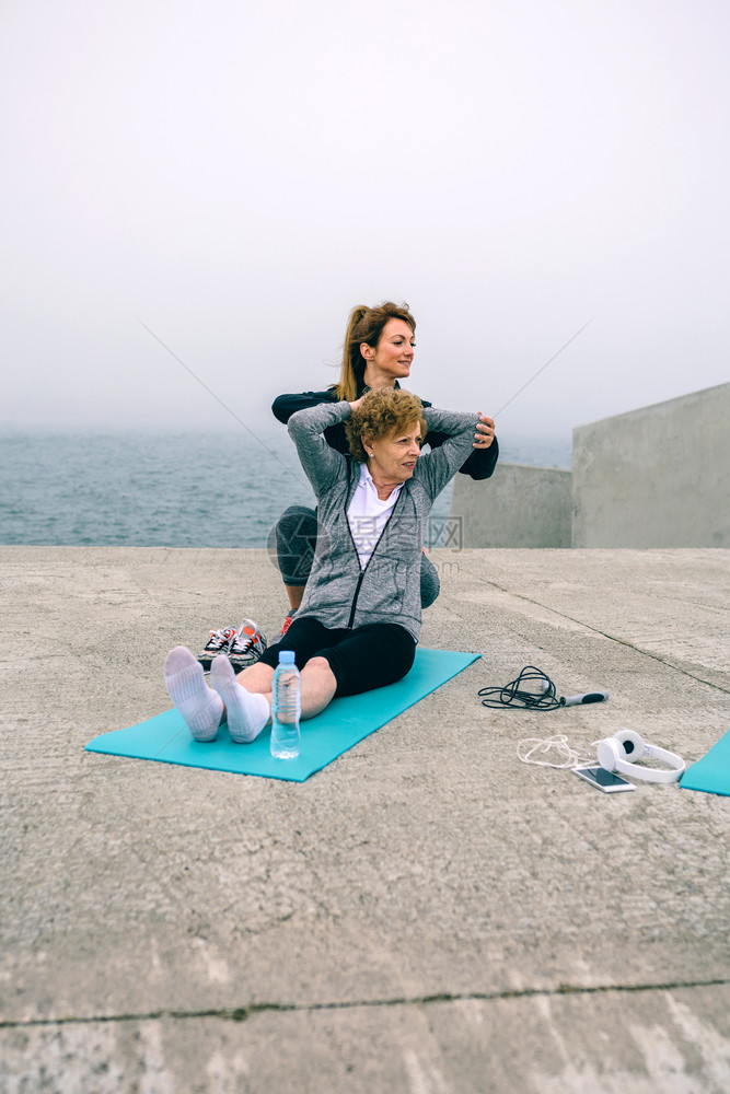 女青年在海岸边的瑜伽垫子上做腿部拉伸运动图片