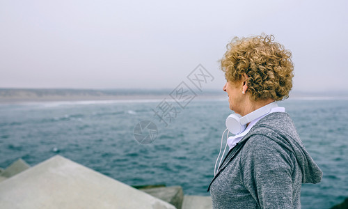 以耳机看着海洋的高级女运动员以耳机看着海洋的高级女运动员看着海洋的高级女运动员背景图片