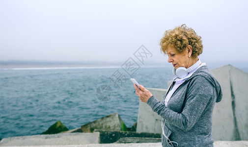 高级女运动员在海上码头看她的智能手机图片