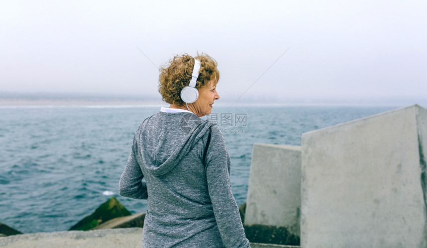 戴耳机的高级运动女员在海码头旁观戴耳机的高级运动女员则在海上码头旁观图片