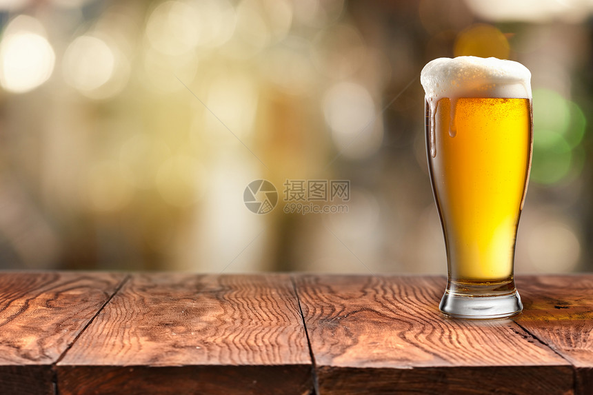玻璃杯的啤酒在木制桌子上加泡沫背景模糊玻璃杯的啤酒放在木制桌子上背景模糊图片