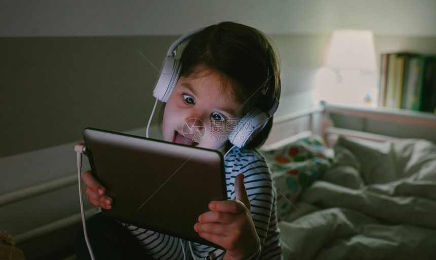 晚上坐在床上玩平板电脑带耳机的女孩图片