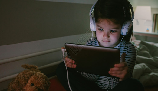 晚上坐在床上玩平板电脑带耳机的女孩图片
