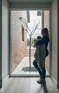 年轻妈妈抱着婴儿在窗边图片