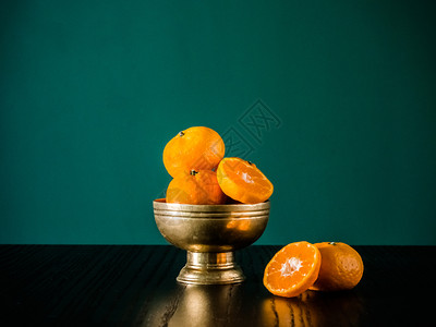 黄铜旧碗中的新鲜橙子黑桌和彩色背景有复制空间图片