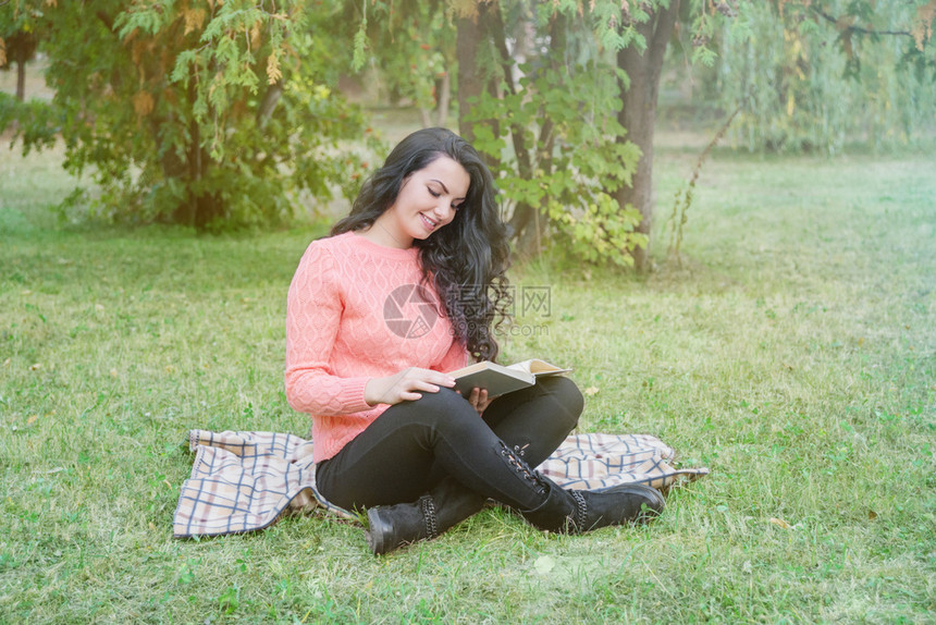 穿着温暖的粉红色毛衣坐在公园里阅读一本书图片