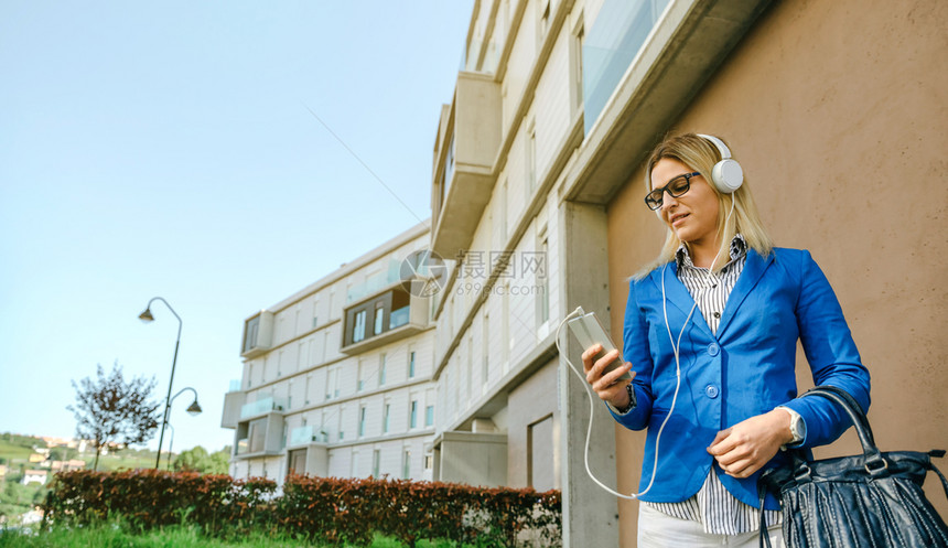 拥有耳机和在街上移动的女商人拥有耳机和移动电话的女商人图片