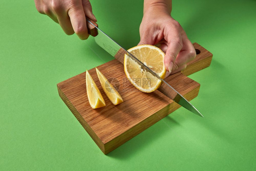 女手切黄熟柠檬在绿色背景下准备自制新鲜鸡尾酒女孩和手砍黄有机柠檬图片