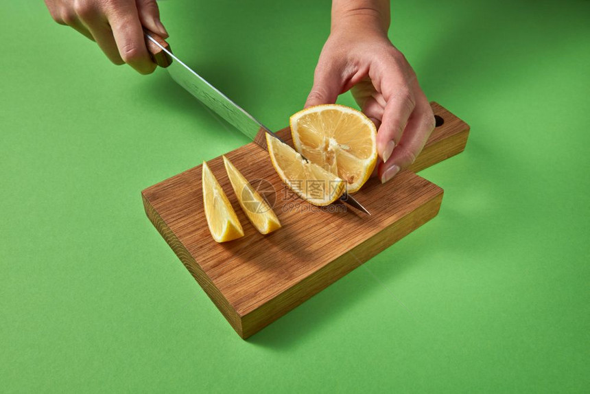 女用手切成多汁的绿色熟石灰切片用于自制健康饮料女和女用手切成一半的绿色熟石灰在绿色背景的木板上切成片图片