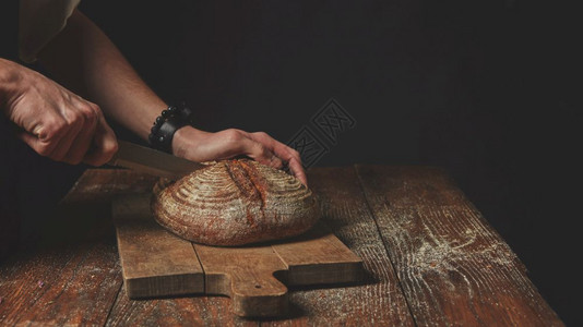 人手在木背景的切割板上了新鲜的圆面包男人和人手切了面包图片