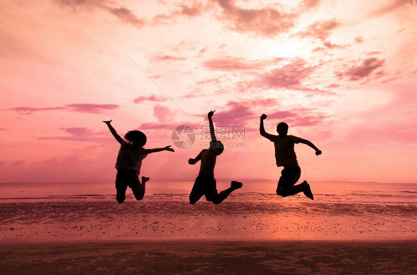 青春快乐的年轻人日落时在海滩上跳跃图片