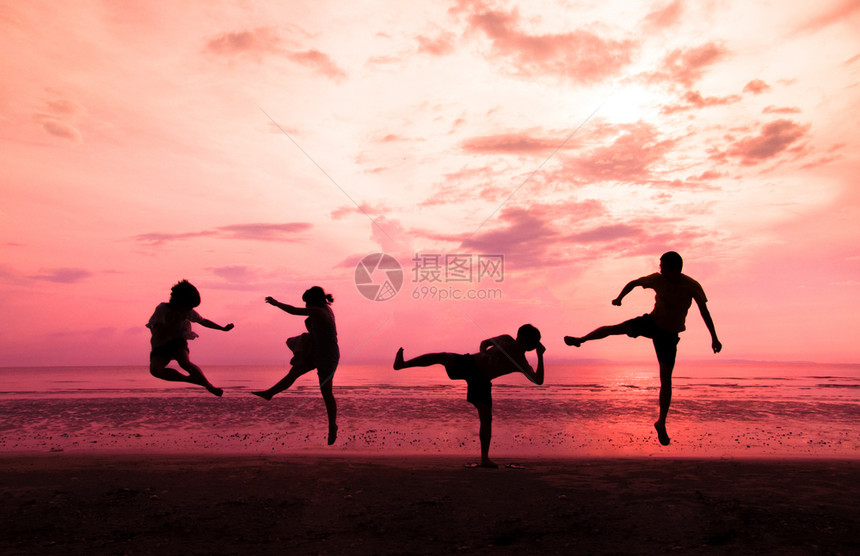 年轻人日落时在海滩上跳跃图片