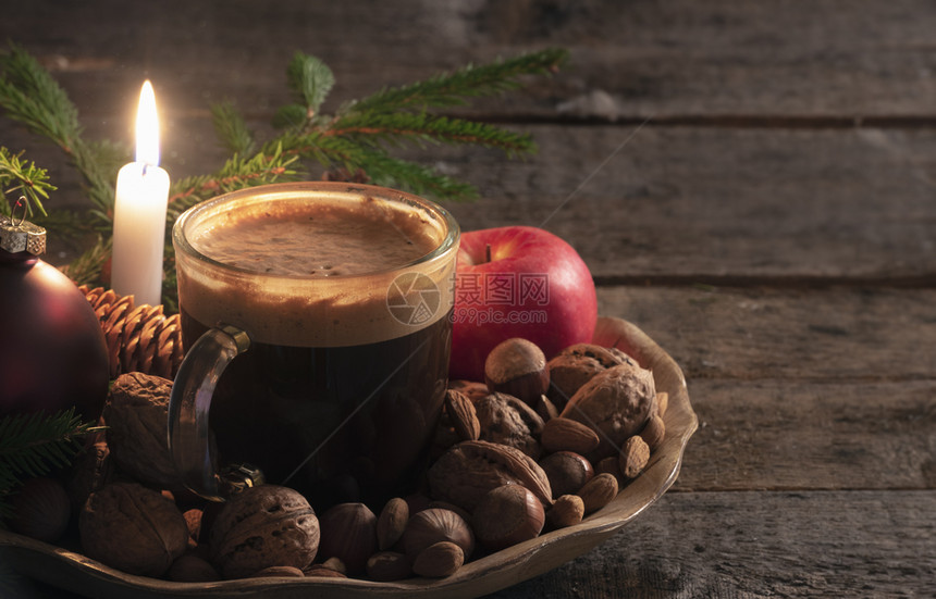 冬天的零食放在木制盘子上还有圣诞节的舞会和树枝坚果苹和一杯咖啡在烛光下生锈的桌子上图片