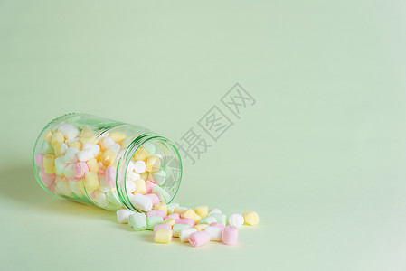 一张玻璃罐被翻倒在绿纸背景上满是细小的多色棉花糖图片