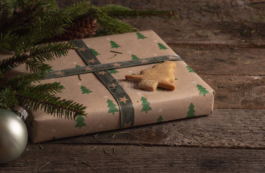 圣诞礼物的概念包在棕色经典纸上的礼物圣诞树形状饼干在顶部和树枝上在一个老旧的木制桌子上图片