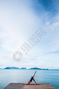 年轻女子在海边的木头码做瑜伽在夏日晴朗的天晴朗在科汉塔克拉比泰兰图片