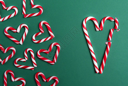 红色的迷你甘蔗以心脏形状排列大的糖果甘蔗以破碎的心形绿色背景图片
