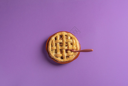 一个苹果馅饼的顶部在一个生锈的瓷器盘里面有一个茶匙紫色背景准备吃甜点平坦的躺下最起码风格背景图片