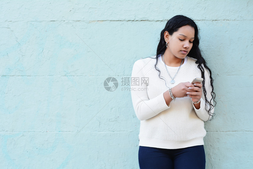 美丽的latin年轻女在街上用智能手机发信息图片