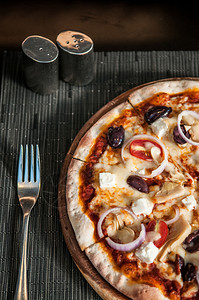 意大利披萨洋葱橄榄番茄奶油酪在晚餐桌上盐辣椒叉子垂直拍摄图片