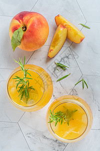 带有冰块和迷迭香叶的自制桃子汁在大理石底的玻璃杯中图片