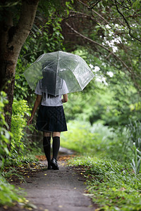 下雨时走在自然行道上带着雨伞行走的亚裔女学生肖像图片