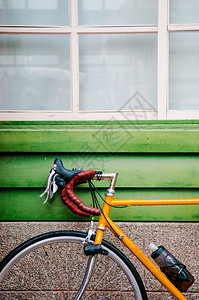 一辆黄色公路自行车靠着绿色木墙停车图片
