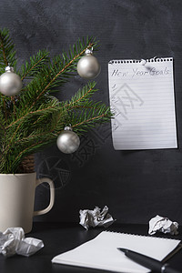 在笔记本上列出新年的目标钉在办公墙上折叠的纸张和桌上松树枝背景图片