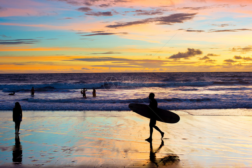 日落时在海滩上走着冲浪板的者图片