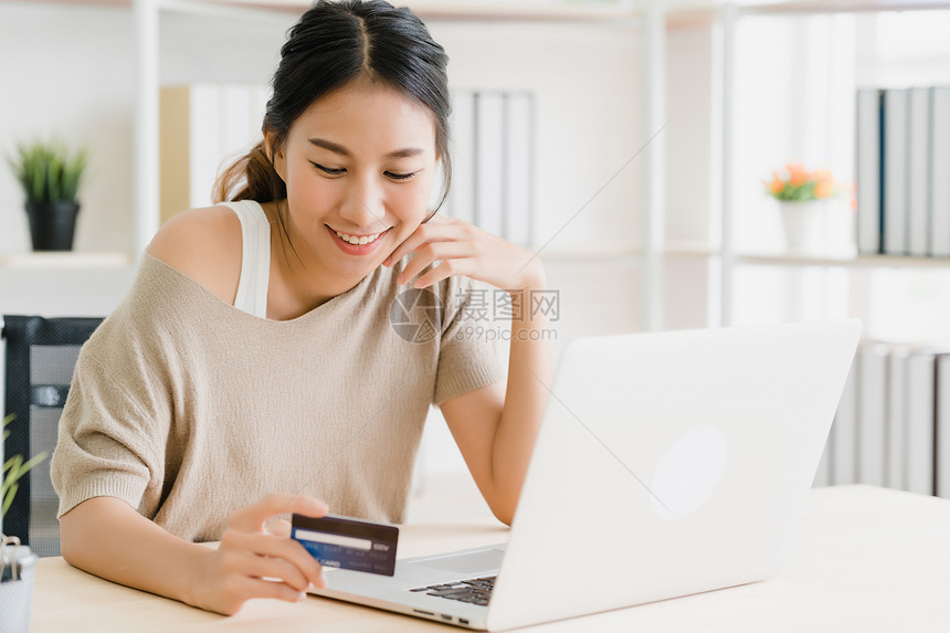 使用计算机或笔记本电脑购买信用卡在线物同时穿着毛衣坐在家中客厅的办公桌上图片