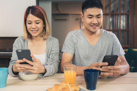 年轻夫妇对坐在餐桌前玩手机图片