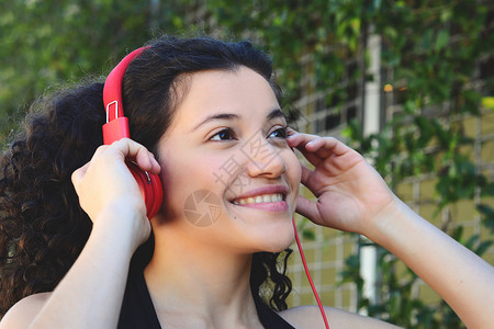 年轻拉丁女人的肖像带着耳机夏季在公园听音乐享受图片