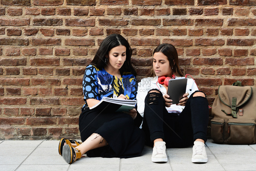 两名女学生正在准备参加城市背景的工作手册和平板电脑考试图片